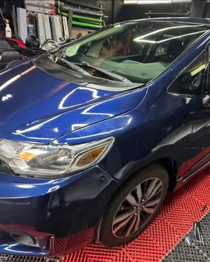 Honda Fit azul en el piso rojo y negro del taller